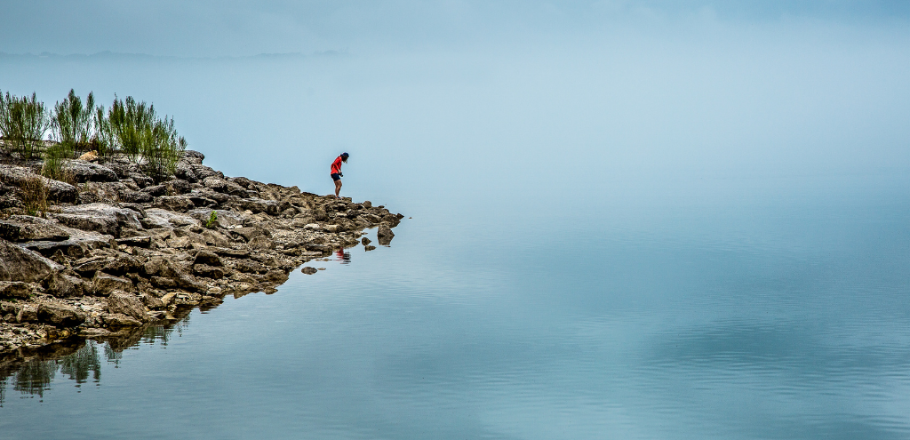 Person standing on the rocky edge of a misty lake