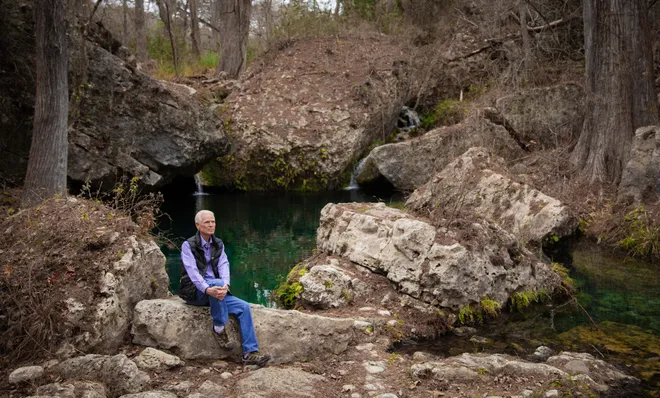 Lew Adams sits on a bank at Roy Creek Canyon’s crystalline pool. The 17-foot-deep pool is surrounded by large boulders and cypress trees and catches water as it flows down the canyon toward the Pedernales River in the Hill Country west of Austin - Sara Diggins/American-Statesman