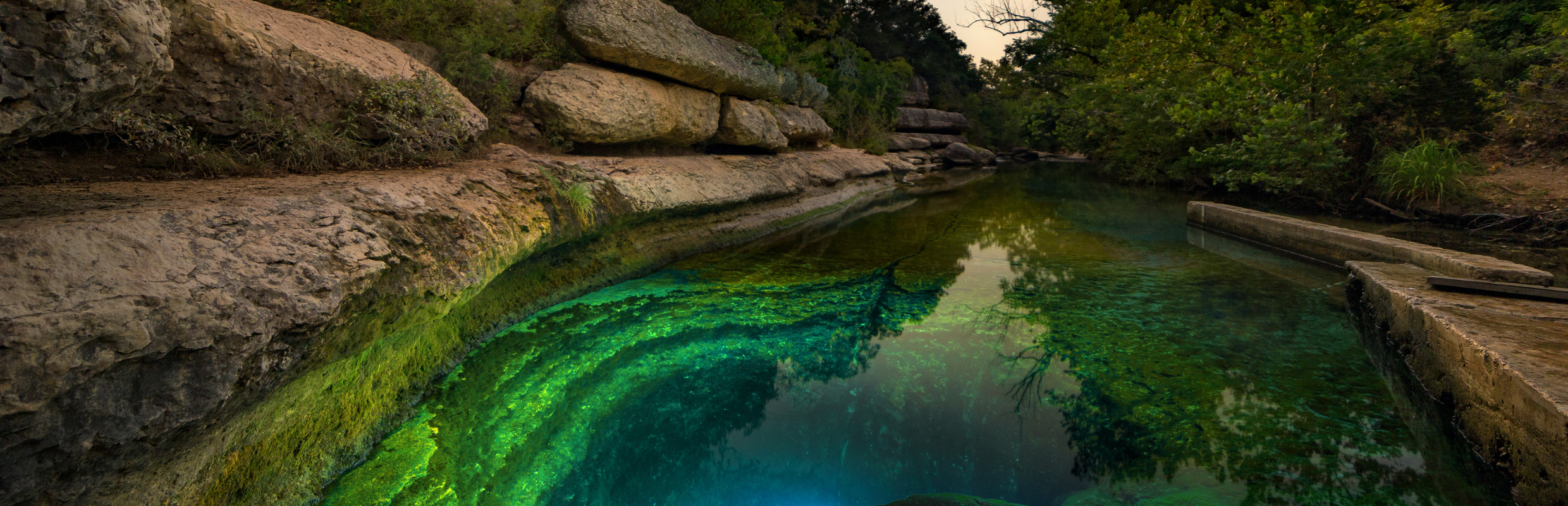The iconic Hill Country Spring - Jacob's Well - is illuminated by a scuba diver at sunset.