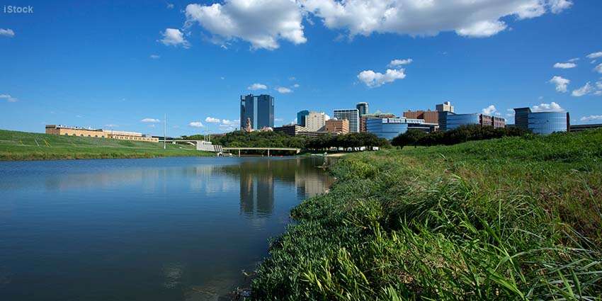 Foreground of water and grassland with the backdrop a series of modern buildings
