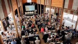 A large crowd fills the seats within a brightly lit barn at the 2023 Leadership Summit
