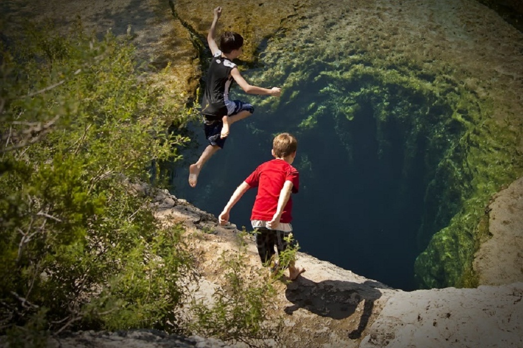Two boys jump into Jacobs Well, a spring in Wimberley, Texas. Photo courtesy of Carl Griffin