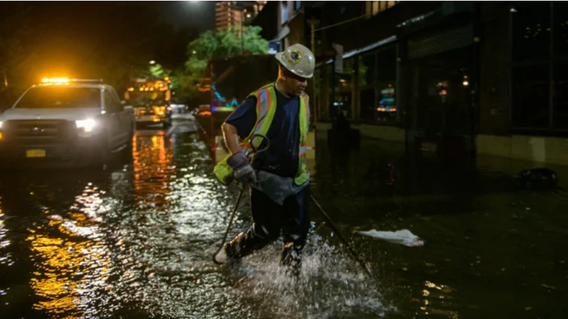A person in a yellow construction vest wades through knee high water in the street