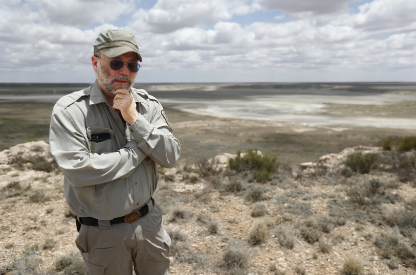 Biologist Jude Smith stands on a bluff overlooking an empty saline lake at the Muleshoe National Wildlife Refuge