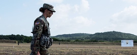 Soldier walks in front of a hill at Camp Bullis