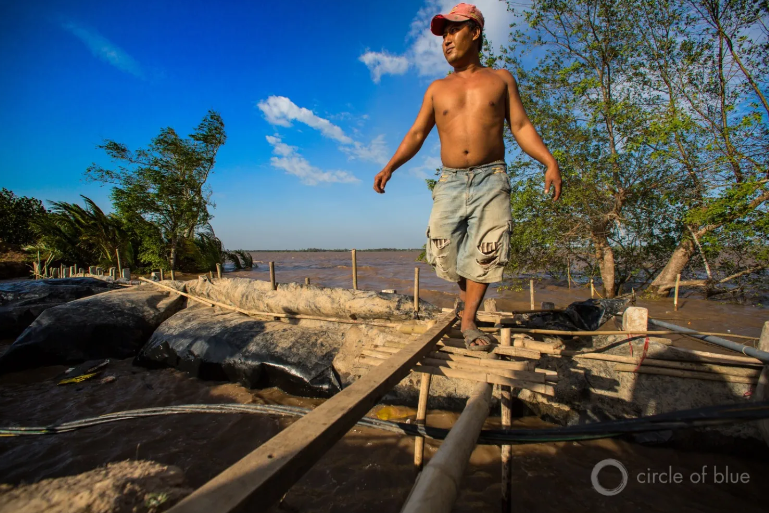 A farmer in the Mekong Delta uses plastic, mud, and sticks to hold back the rising sea.