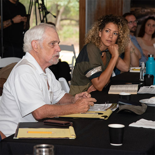 Image shows a man in conversation with speakers, while a woman looks on attentively in the background. 