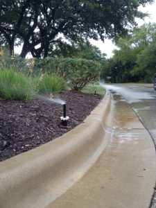 Sprinklers shown spraying water onto landscaping as it rains.